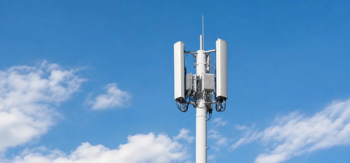 5G base station tower with sector panel antennas against a blue sky — telecommunications industry